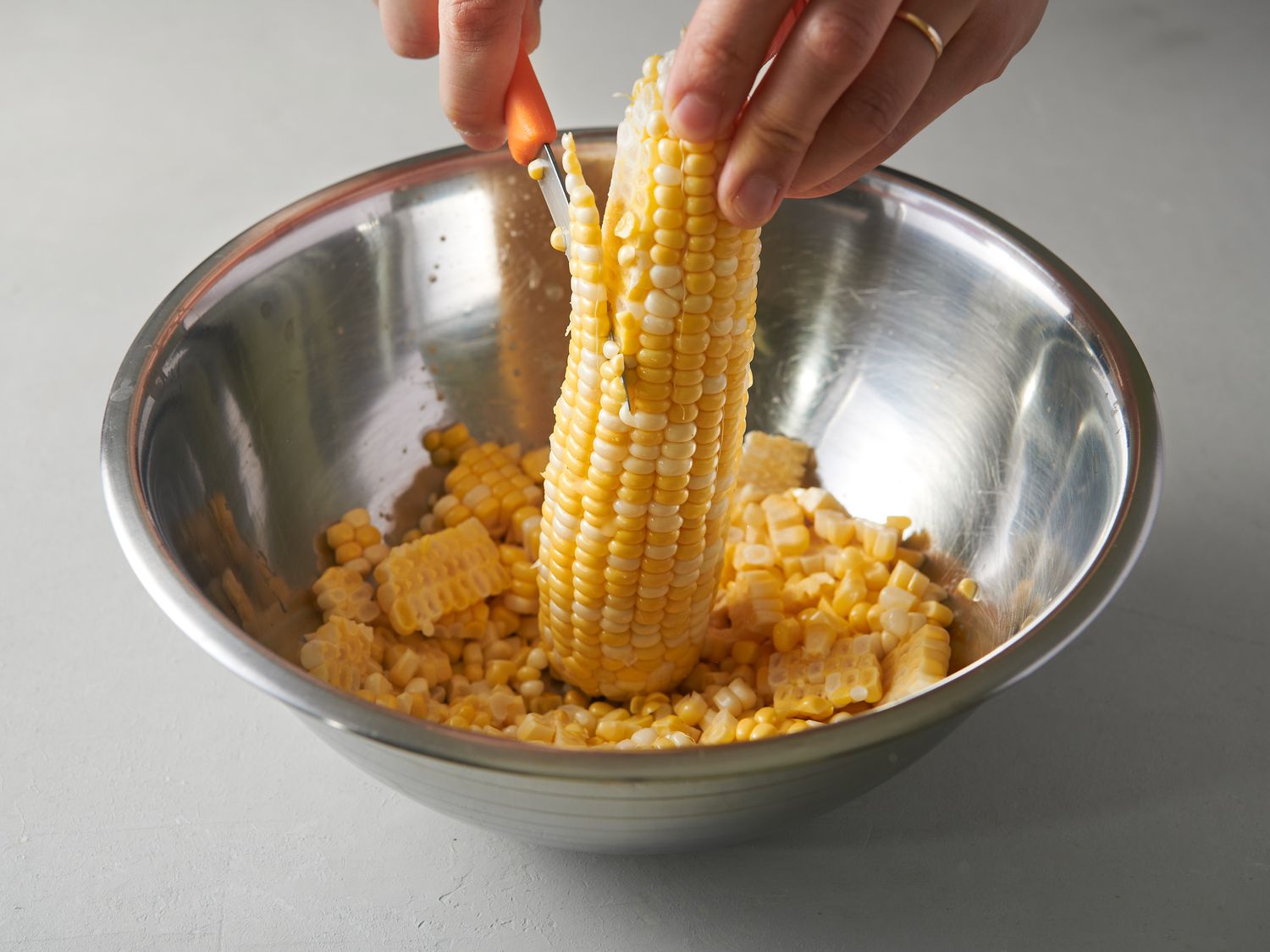 Holding corn cob upright in a large bowl and cutting off kernels with a sharp knife