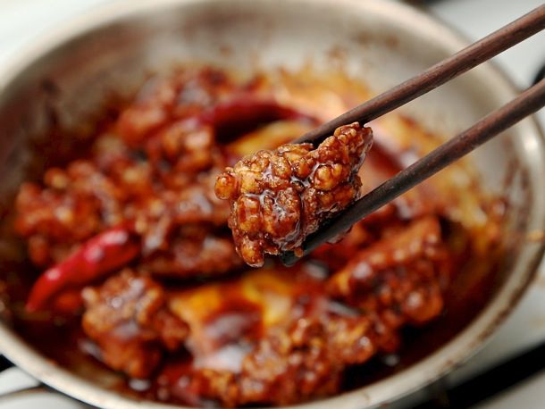 Using chopsticks to hold up a piece of General Tso's chicken above skillet of chicken.