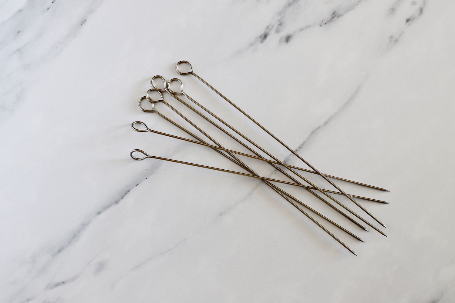 a handful of stainless steel skewers on a marble surface