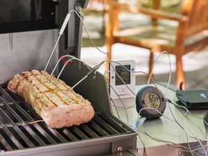 two thermometers on a grill table taking the temperature of a piece of meat cooking on the grill