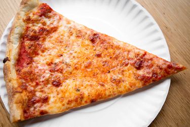 A slice of New York style cheese pizza on a white paper plate.