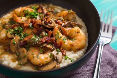 A bowl of shrimp and grits with bacon, chopped herbs, and mushrooms.