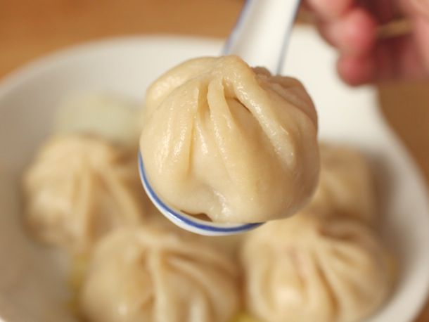A large soup spoon cradles a xiao long bao dumpling.