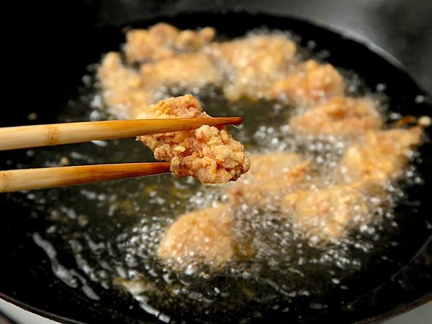 Holding a piece of fried chicken with chopsticks above wok filled with hot oil and frying chicken.