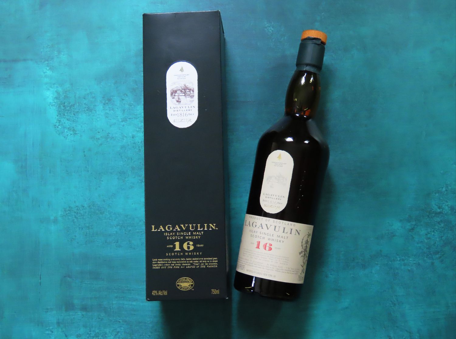 a bottle of Lagavulin beside its box on a blue surface