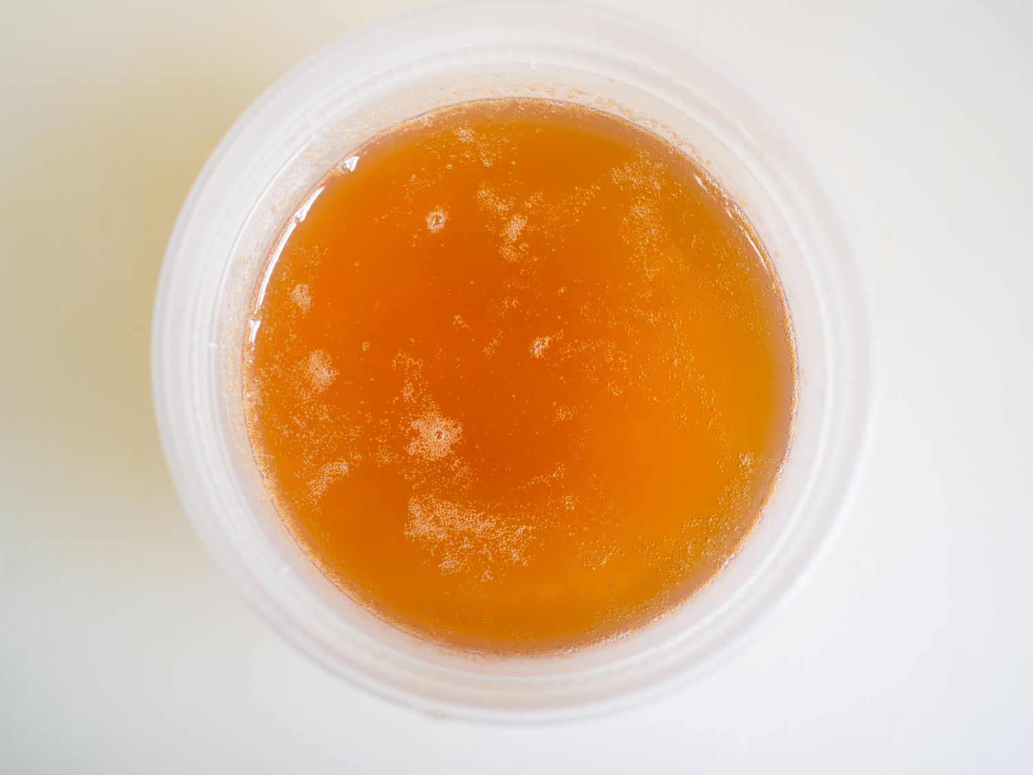 Overhead view of a deli container filled with dark, golden schmaltz.