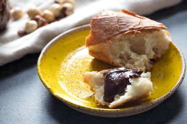 Homemade Nutella spread on a piece of baguette on a yellow plate.