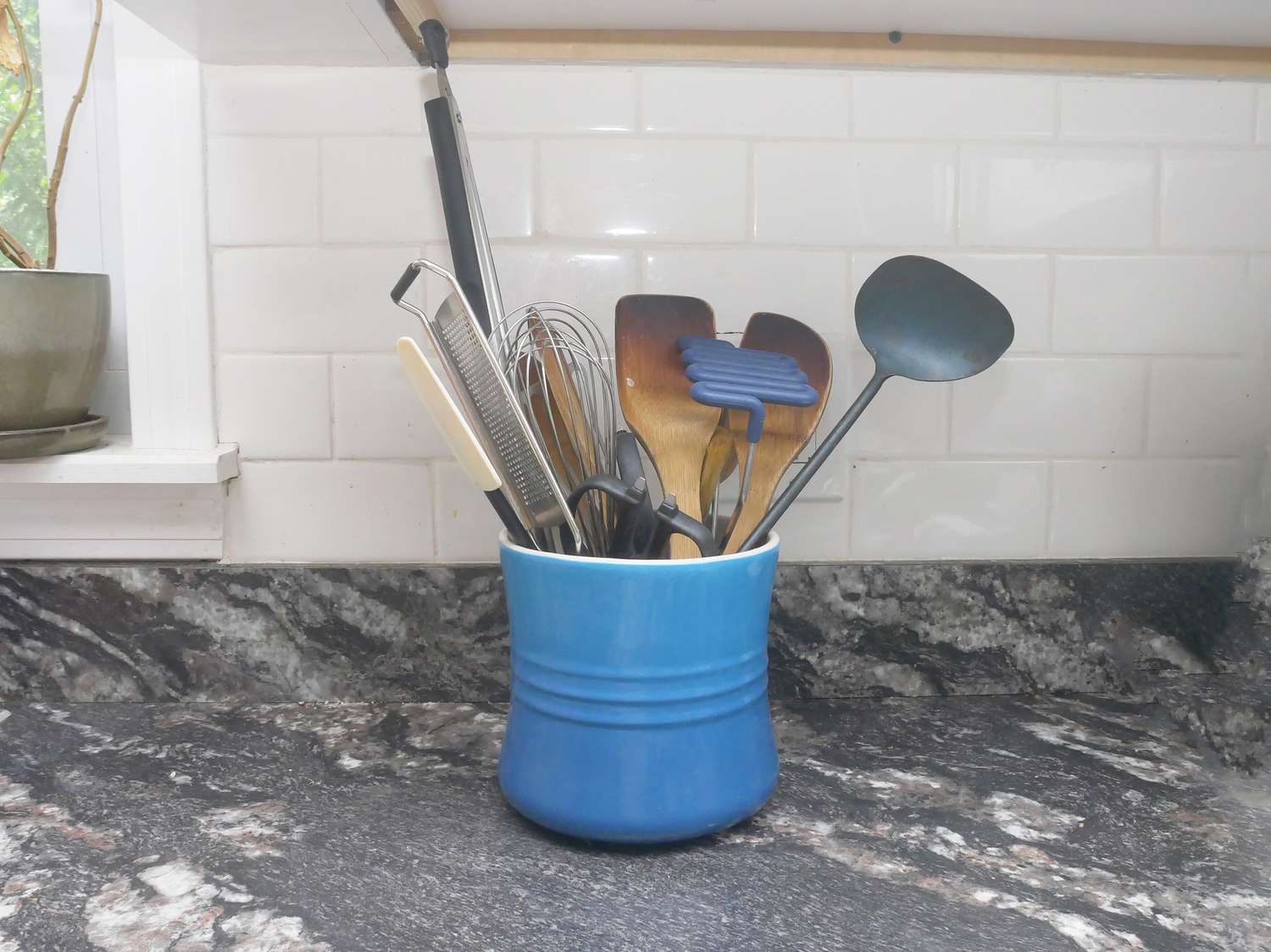 a blue utensil crock full of wooden spoons and spatulas on a dark marble counter