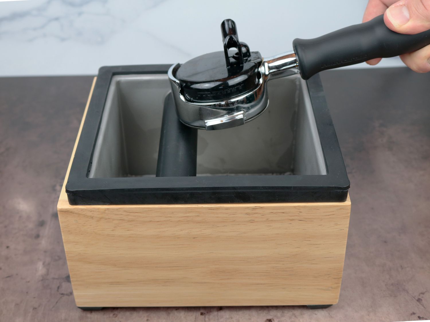a knock box with an off center bar with a portafilter tapping the rubber bar