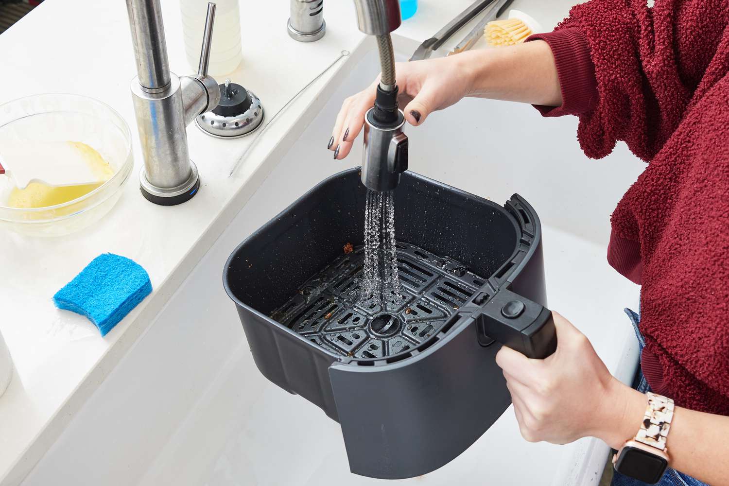 a person washing the basket of an air fryer in the sink