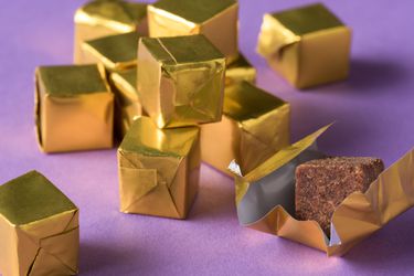 Closeup of a pile of gold foil-wrapped bouillon cubes. One has been unwrapped to reveal the cube itself.