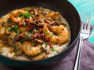 A bowl of shrimp and grits with bacon, chopped herbs, and mushrooms.