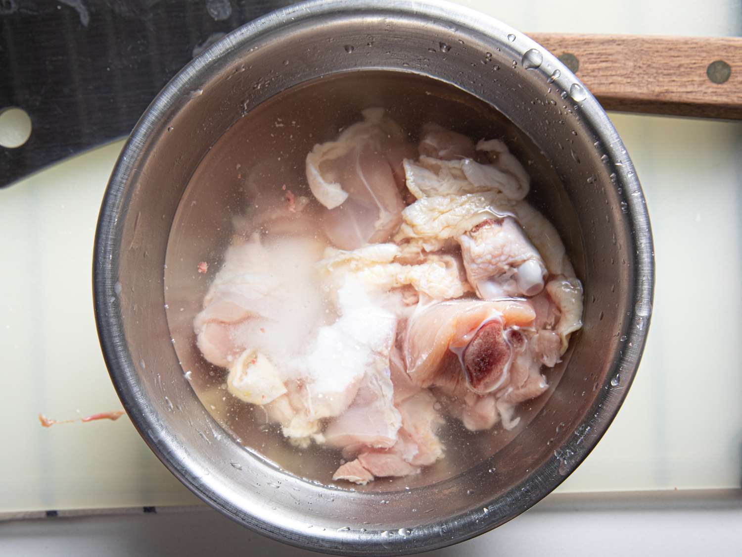 Chicken sitting in water in a stainless steel bowl.