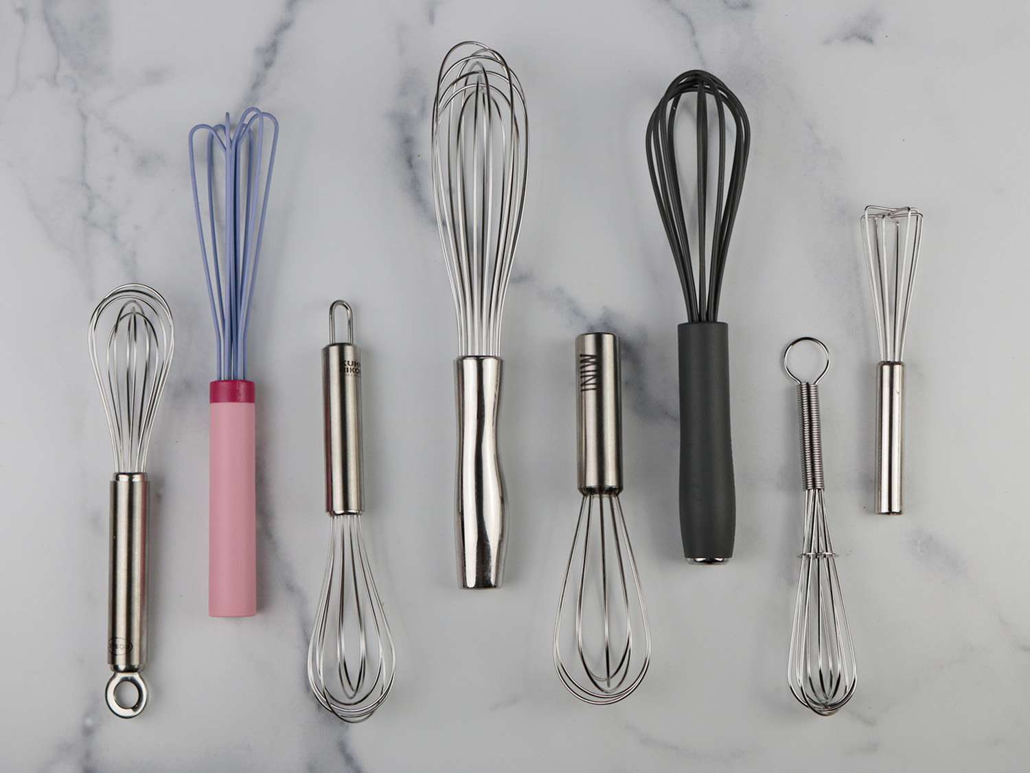 eight different miniature whisks on a marble background