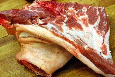 A raw pork brisket on a cutting board.