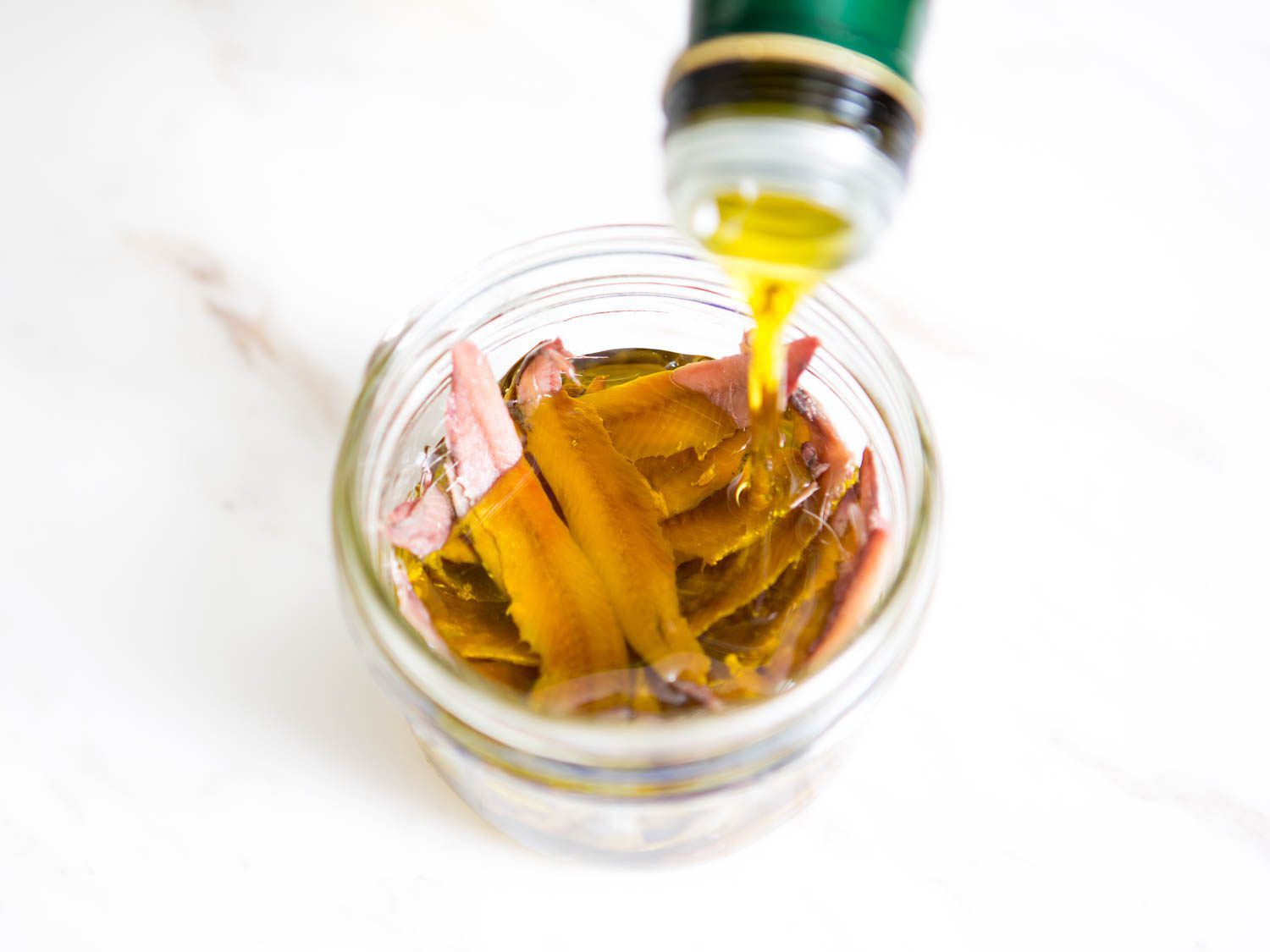 Salt-packed anchovy fillets, rinsed and deboned, are placed in a small canning jar and submerged in olive oil.