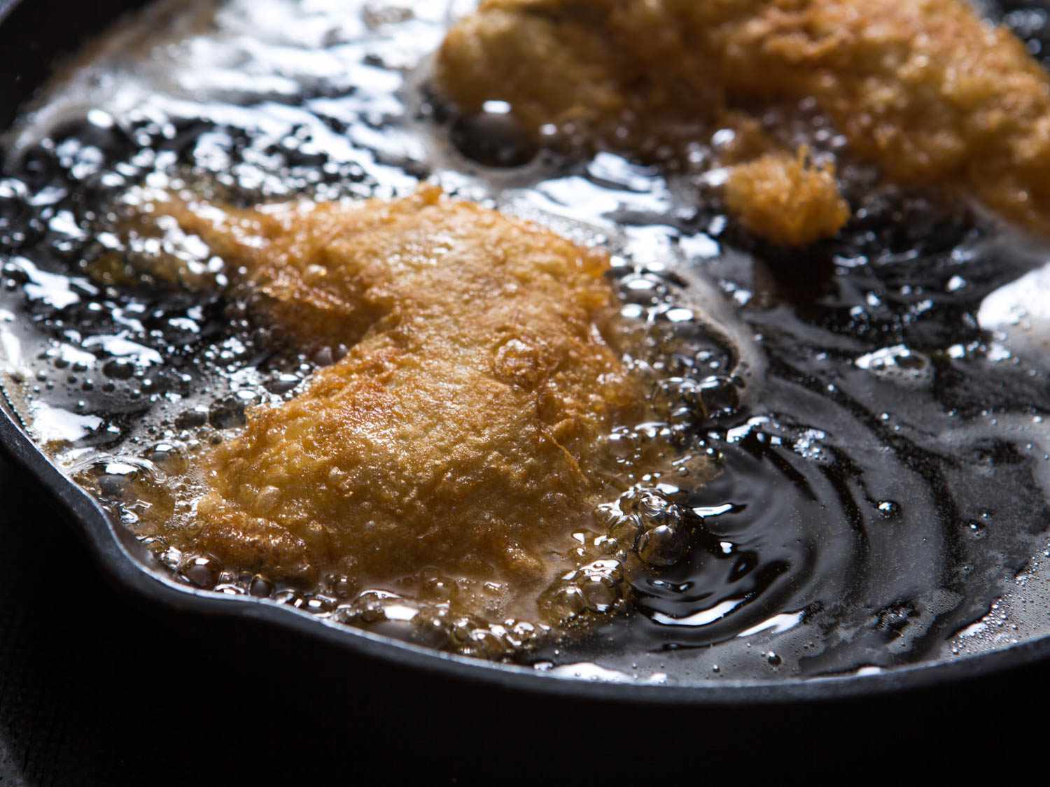 Chicken frying in oil in a cast-iron skillet