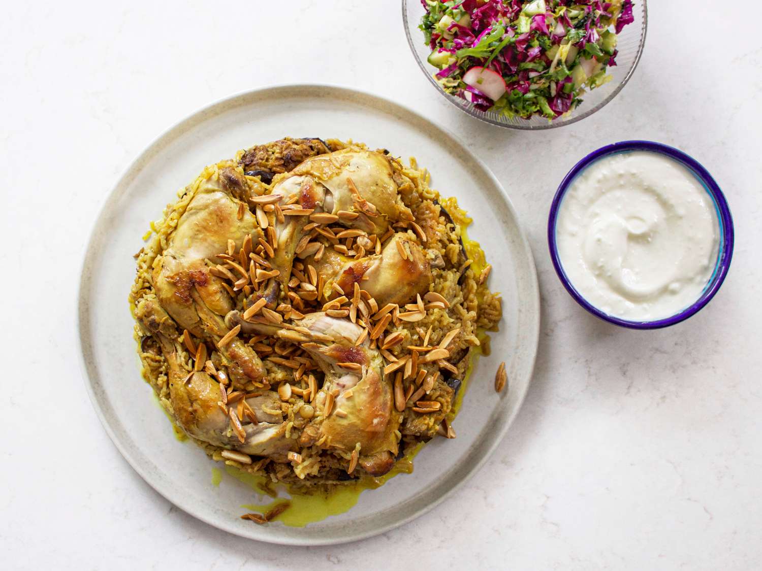 Maqlubeh被放在一个白色的盘子里，旁边放着一碗酱汁和一份小沙拉