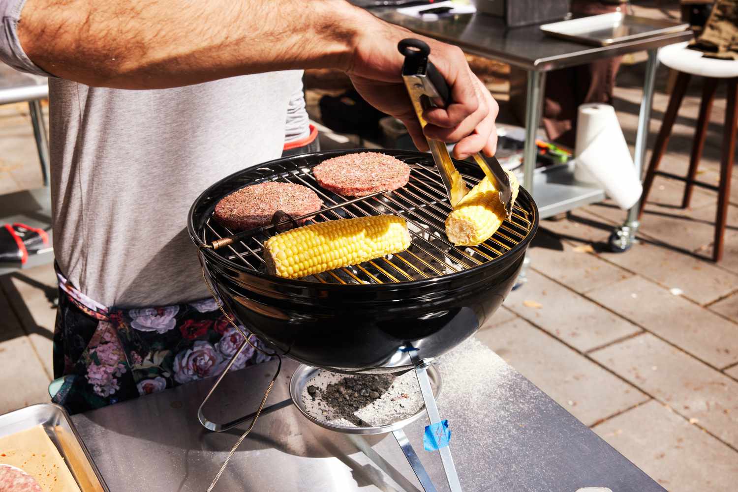 a person using tongs to flip corn on a portable charcoal grill