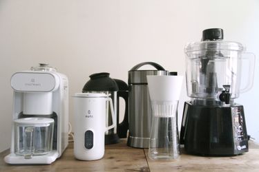 a variety of nut milk makers lined up on a wooden countertop