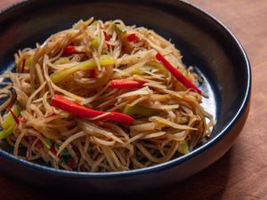 A plate of very thin strands of stir-fried potato and red and green pepper; the potato looks softened but not limp, and is a beige color that hints at the sauce it absorbed in the wok.