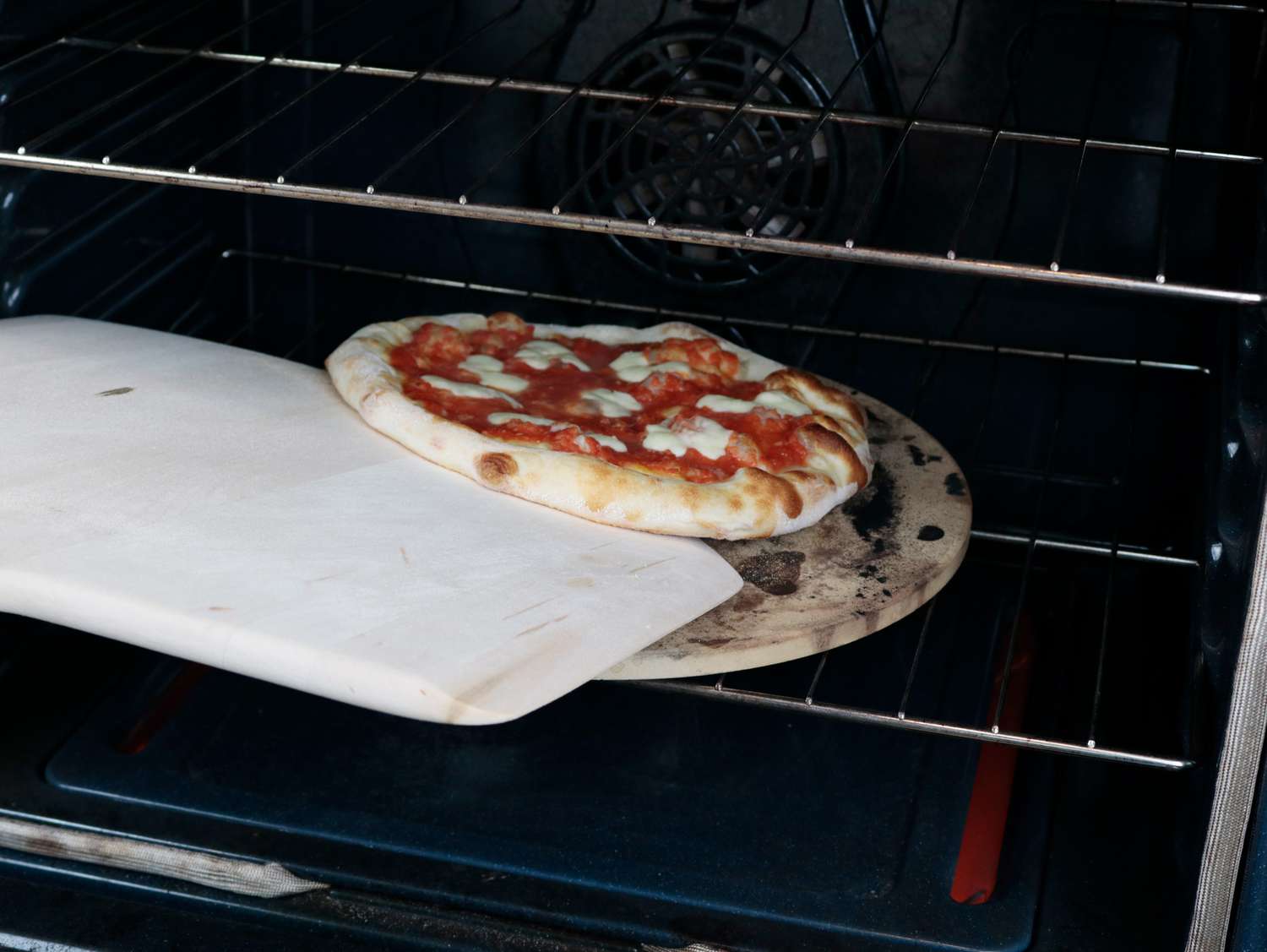 a wooden peel tries to turn a pizza in an oven