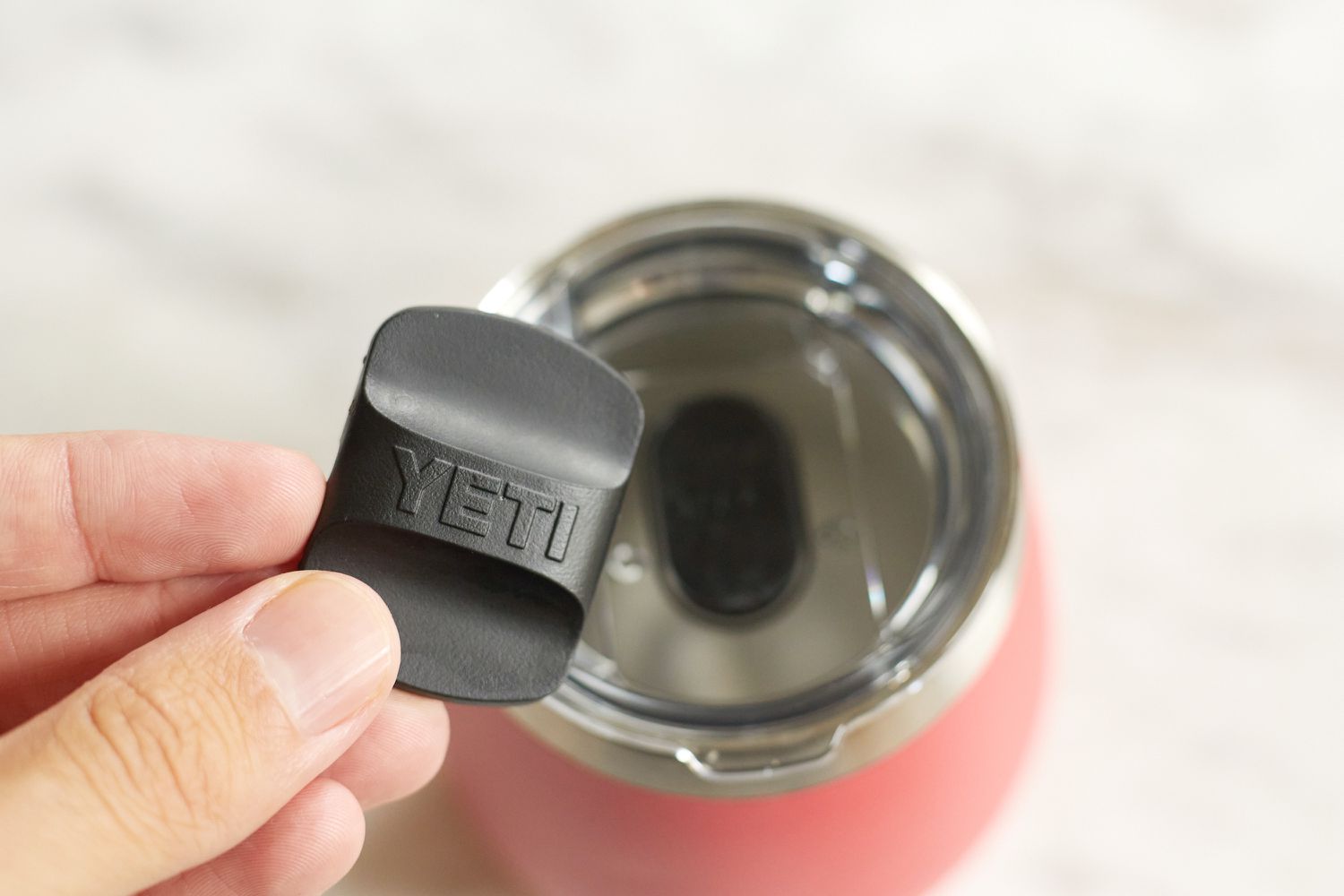 a wine tumbler's slider lid grasped between someone's fingers