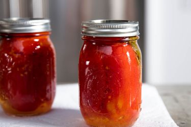 Two quart jars of canned tomatoes placed on a paper towel, gleam in the sunlight.