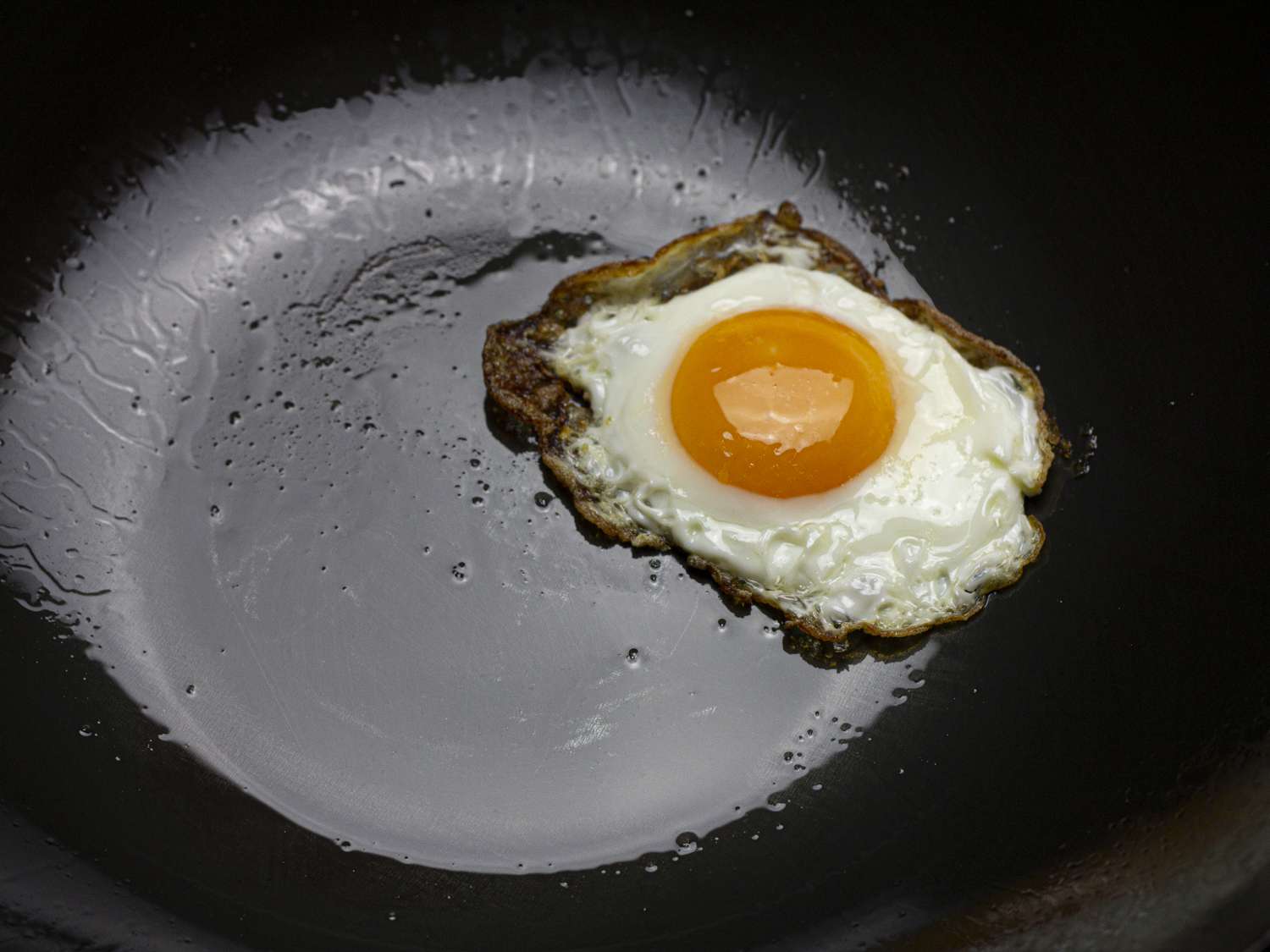 A closeup of a fried egg in a well-seasoned wok.