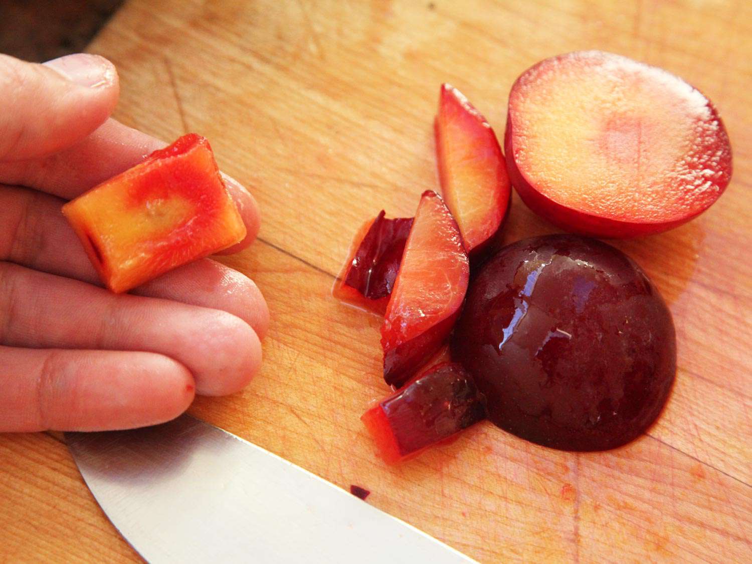 一只手拿着一个李子核，周围有一些水果，旁边的木板上放着切好的水果