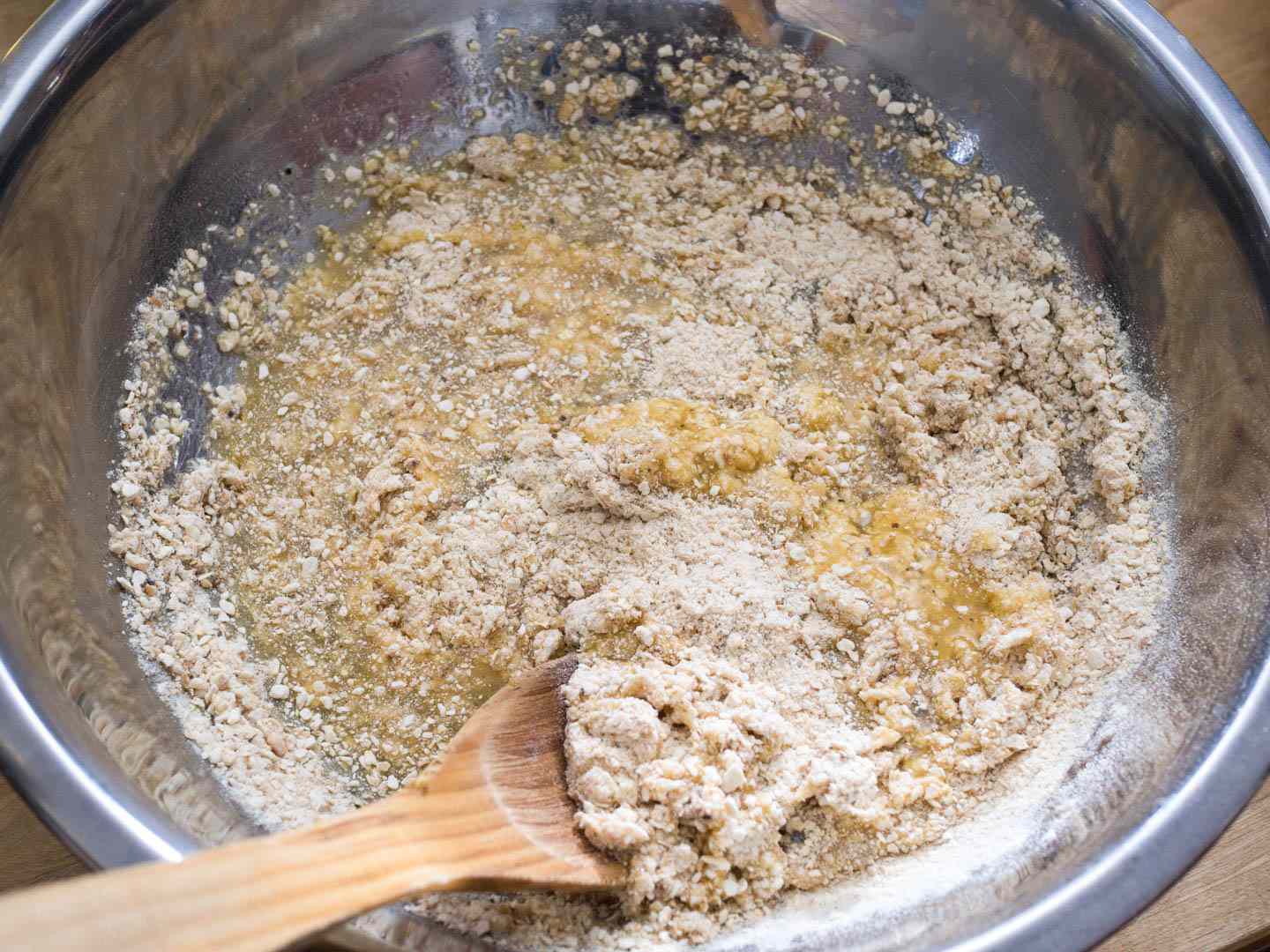 Matzo meal and the rest of the dry ingredients and the egg-seltzer-schmaltz mixture are being stirred together with a wooden spoon in a mixing bowl.
