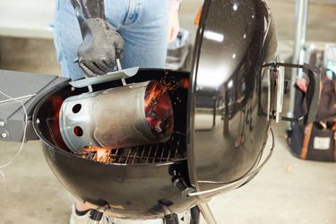 A person using a chimney starter to pour hot coals into a charcaol grill