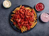 A large platter of salchipapa (french fries with sliced hot dogs piled on top) and a few dipping sauces alongside