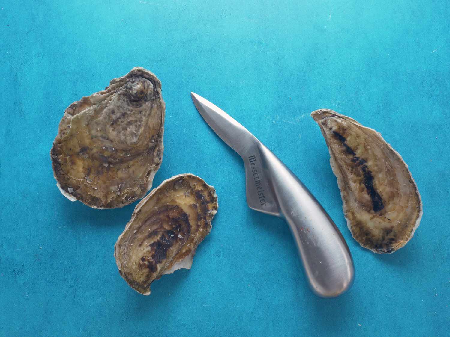 Messermeister oyster knife next to three oysters