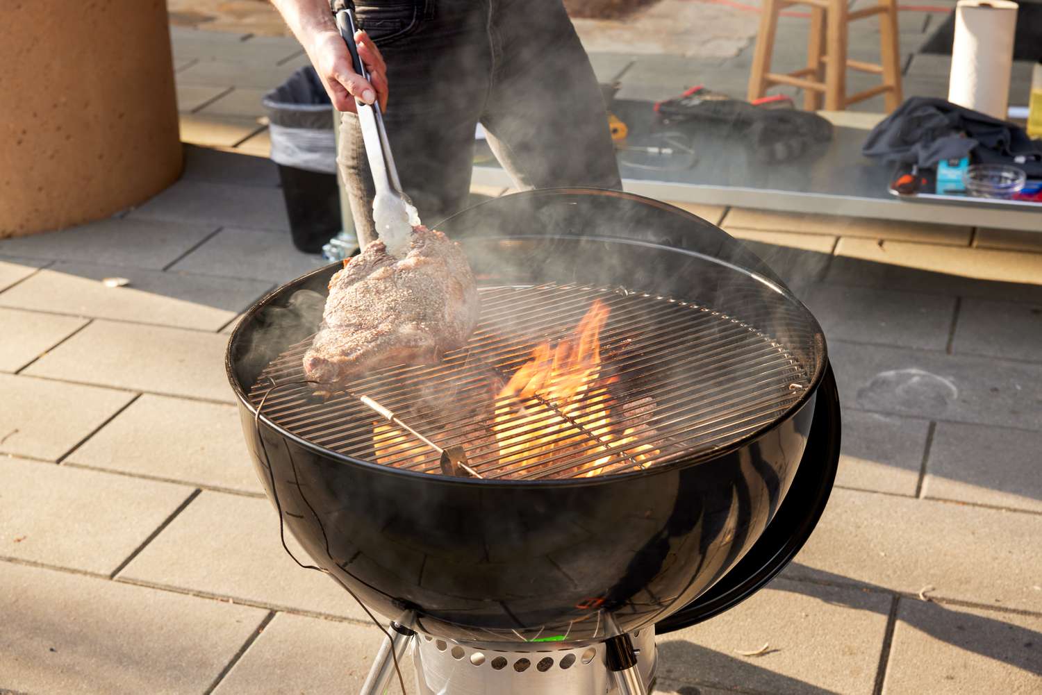 A person using tongs to flip a steak on a charcoal grill