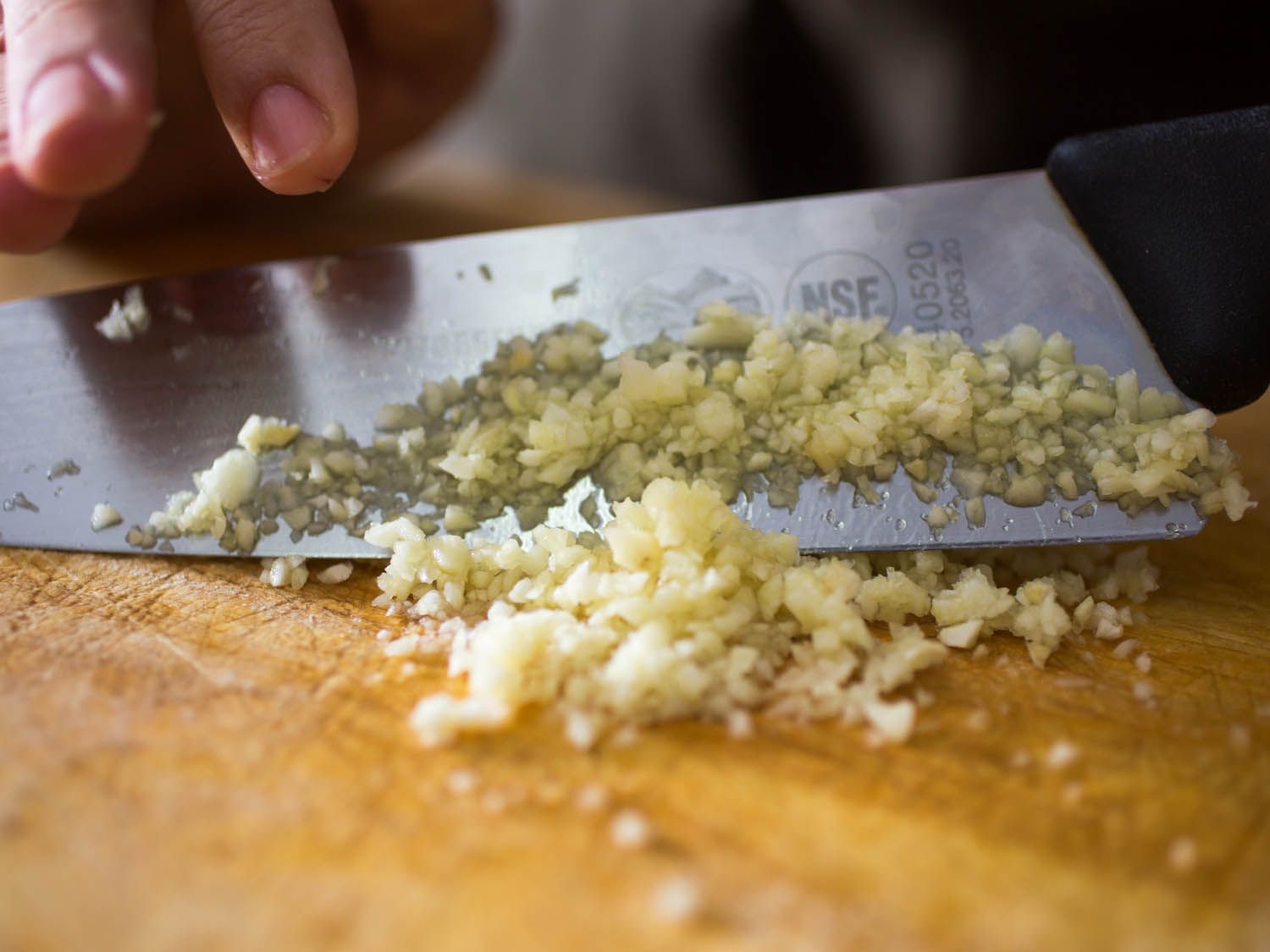 A closeup shot of minced garlic on the blade of a knife.