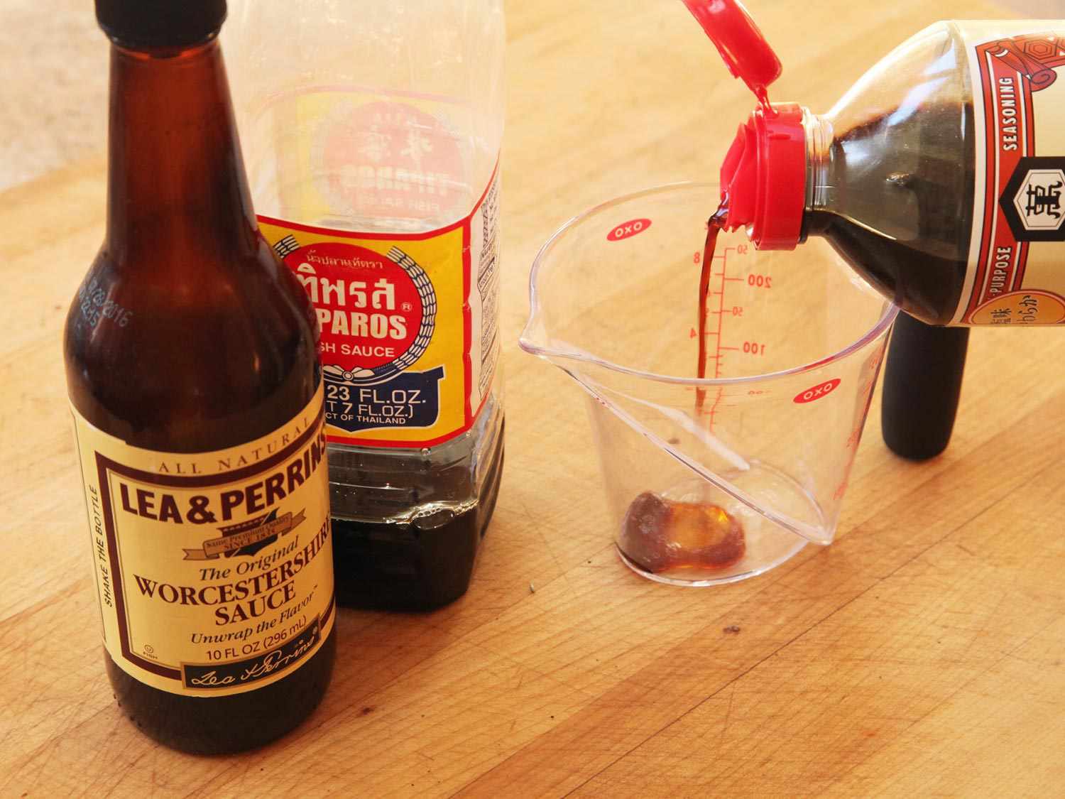 一瓶瓶伍斯特沙司和鱼露放在量杯旁，酱油正被倒进量杯里。