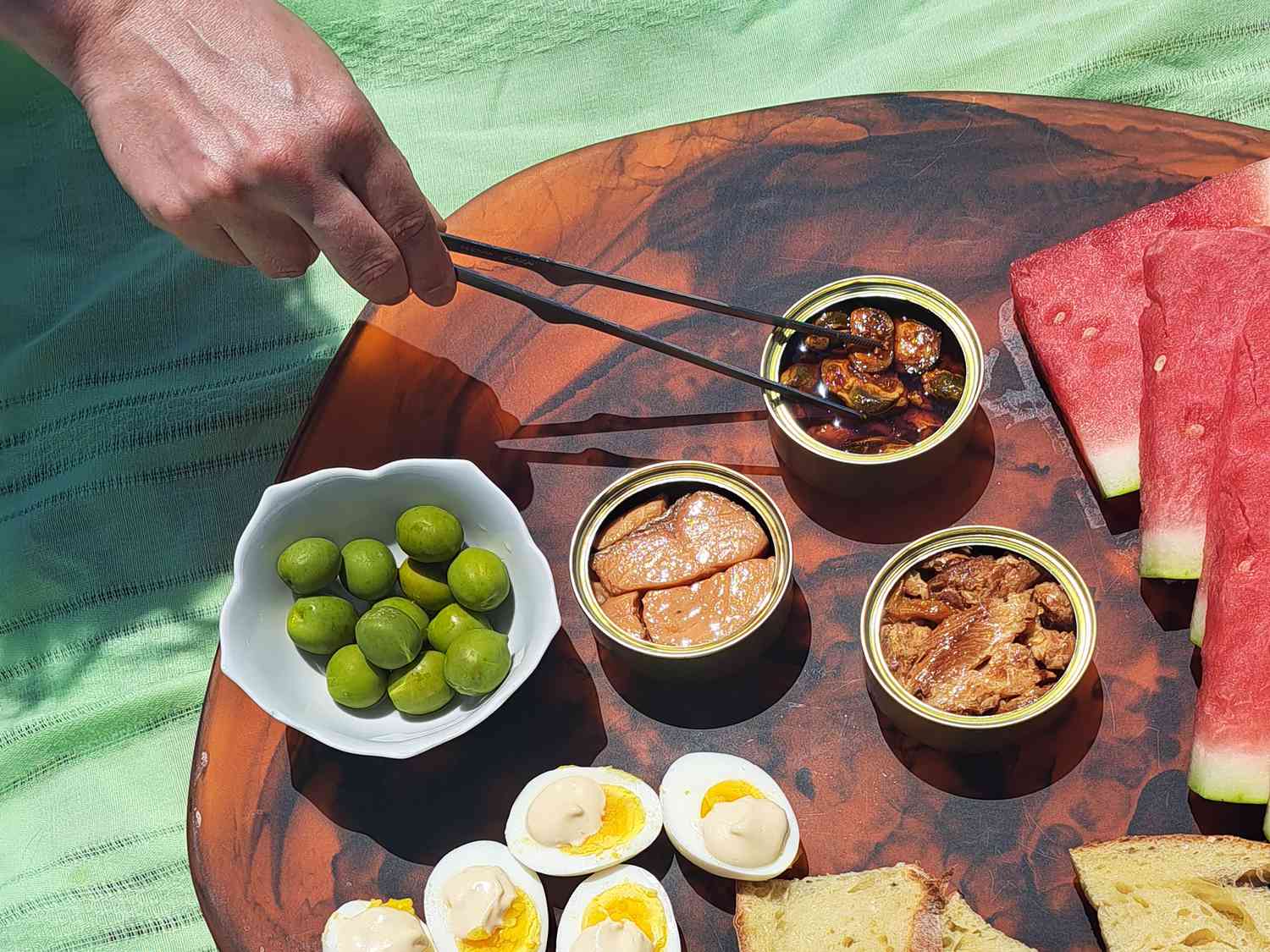 a hand using tweezers to grab a mussel from a tin