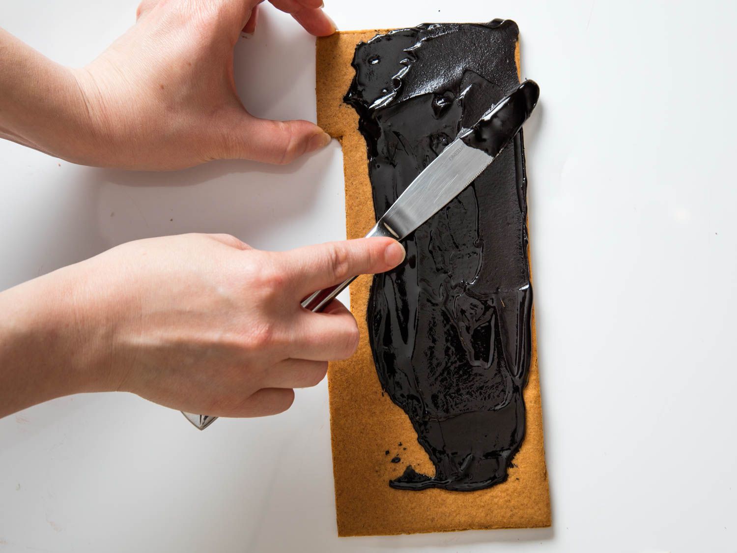 Painting black frosting over a piece of gingerbread to make a haunted-house roof