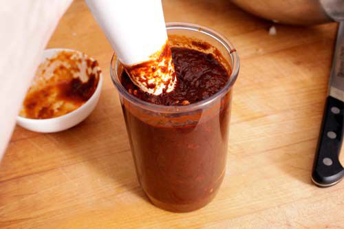 Immersion blender in glass jar blending together dark red chile sauce