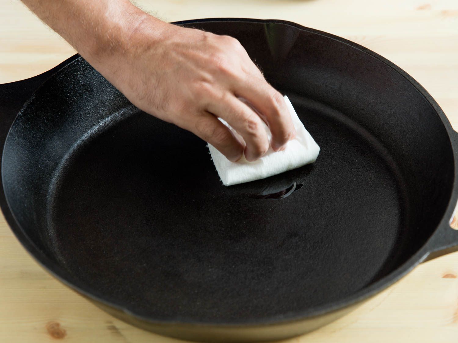 一只手拿着纸巾，用油擦拭铸铁煎锅的内部