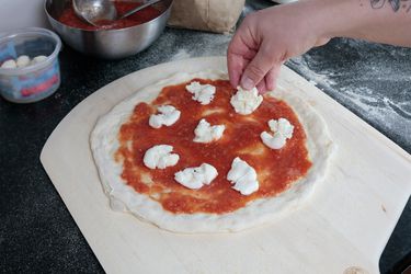 一只手在木制披萨皮上的披萨上浇上了意大利干酪