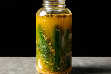 Open jar of homemade pickled cucumbers in brine, viewed from side.