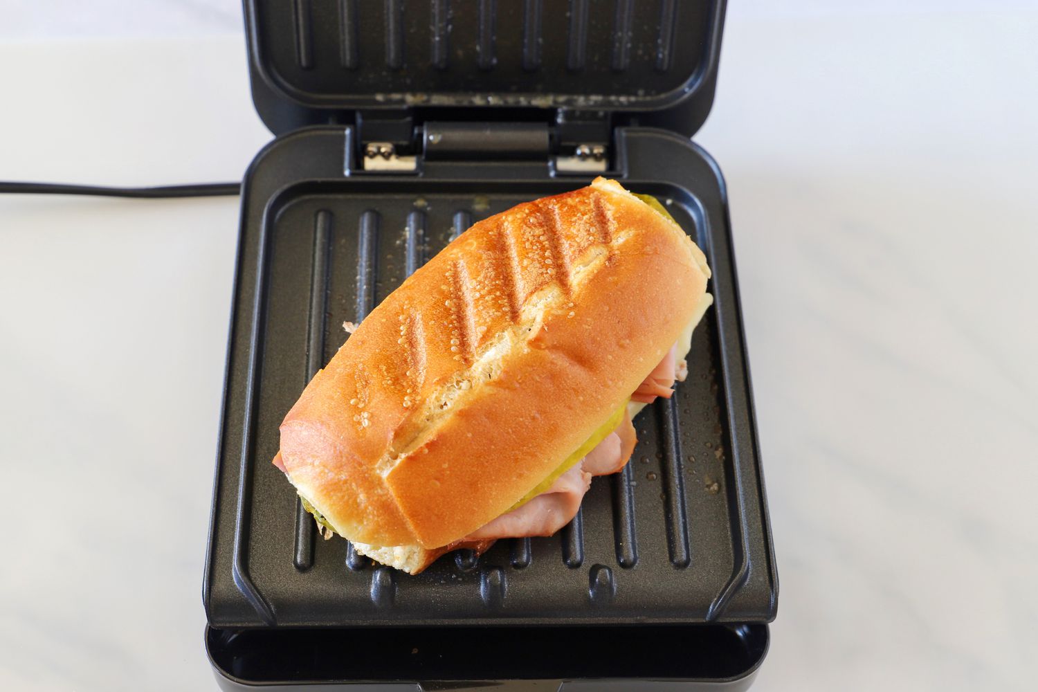 a small panini press with a sandwich on its grates and its lid open