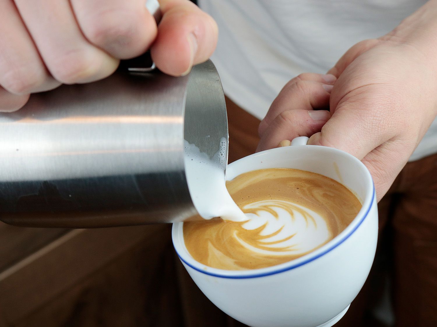hands holding a milk pitcher latte cup pouring latte art onto the surface