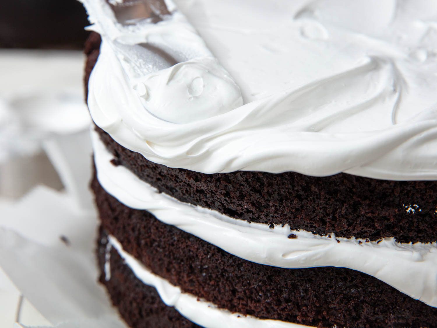用偏移抹刀在三层巧克力蛋糕上涂抹7分钟蓬松的糖霜，黑的一面仍然暴露在外面