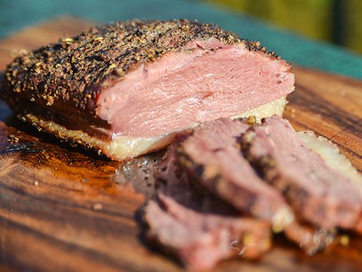 A sliced duck breast coated in a crust of spices resting on a wooden cutting board