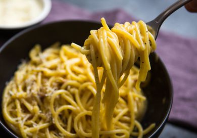 Close-up of spaghetti carbonara twirled on a fork above a serving bowl.