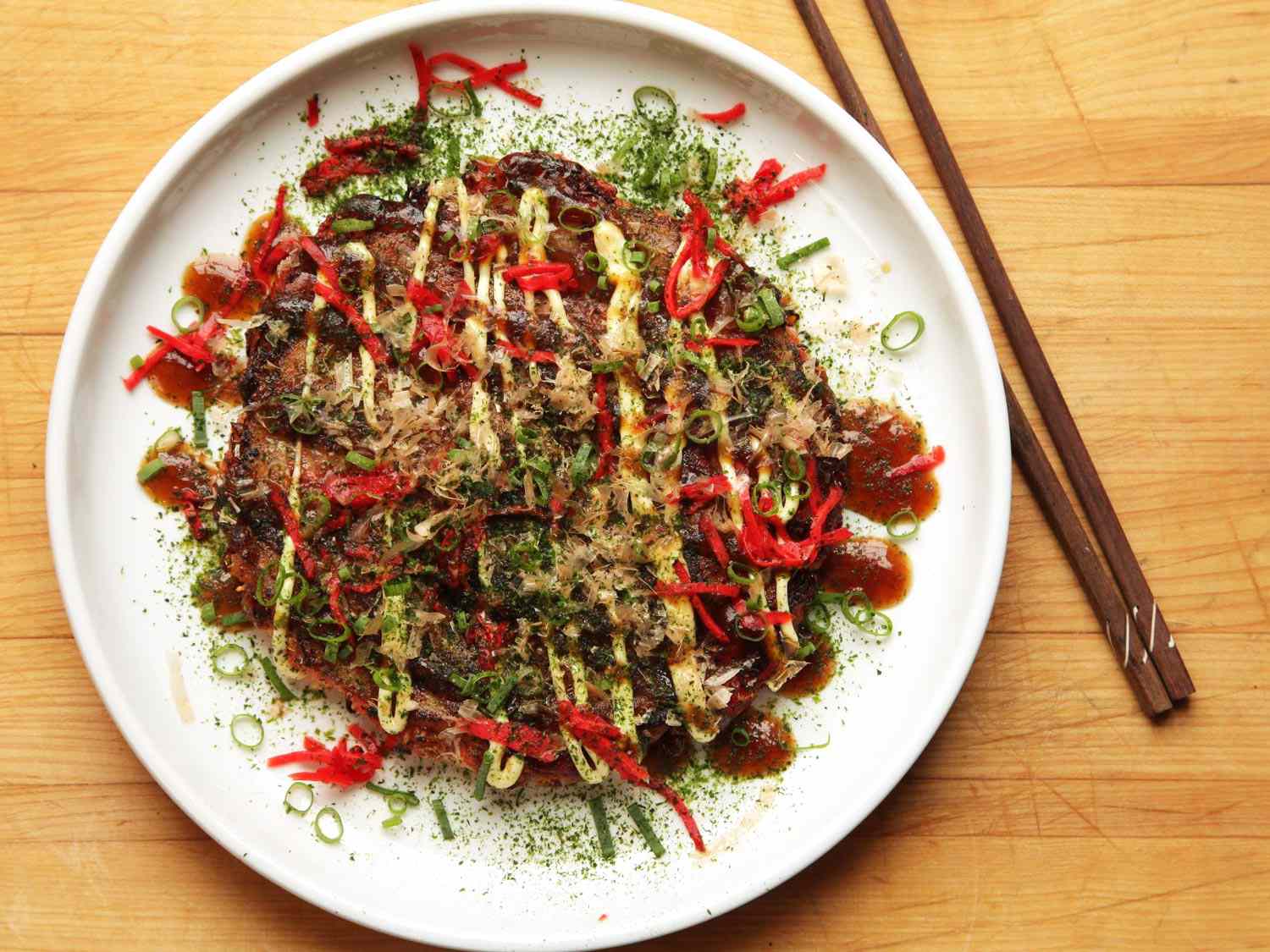okonomiyaki，一种日式白菜煎饼，放在白色盘子里，旁边放着筷子。