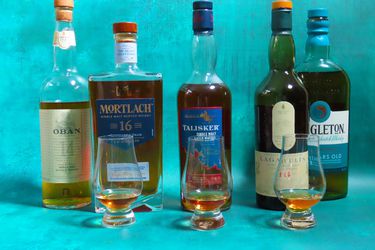 multiple bottles of whisky and whisky tasting glasses on a blue surface